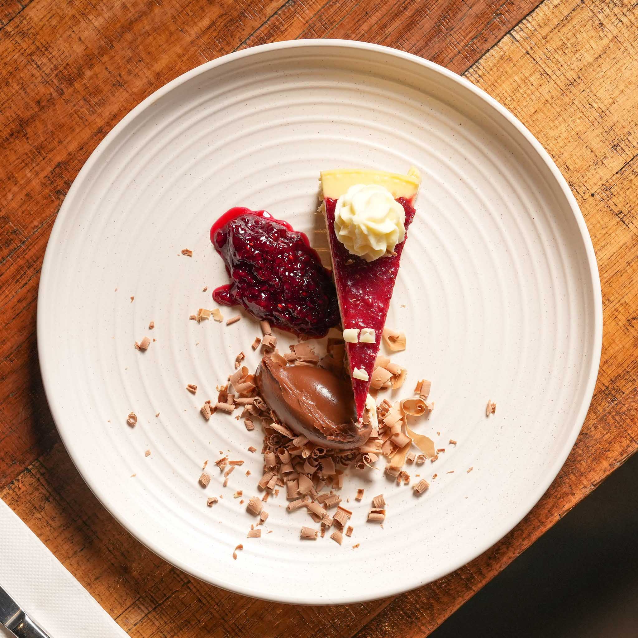 New York Raspberry Cheesecake | Creamy New York Cheesecake Topped With Raspberry Compote, White Chocolate Curls And Ganache Peaks | $16.80